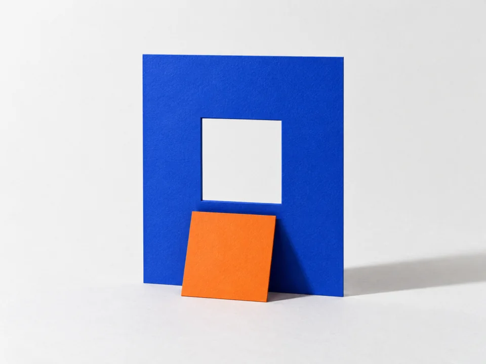 An orange square card in front of the matching window cut in a cobalt sheet.
