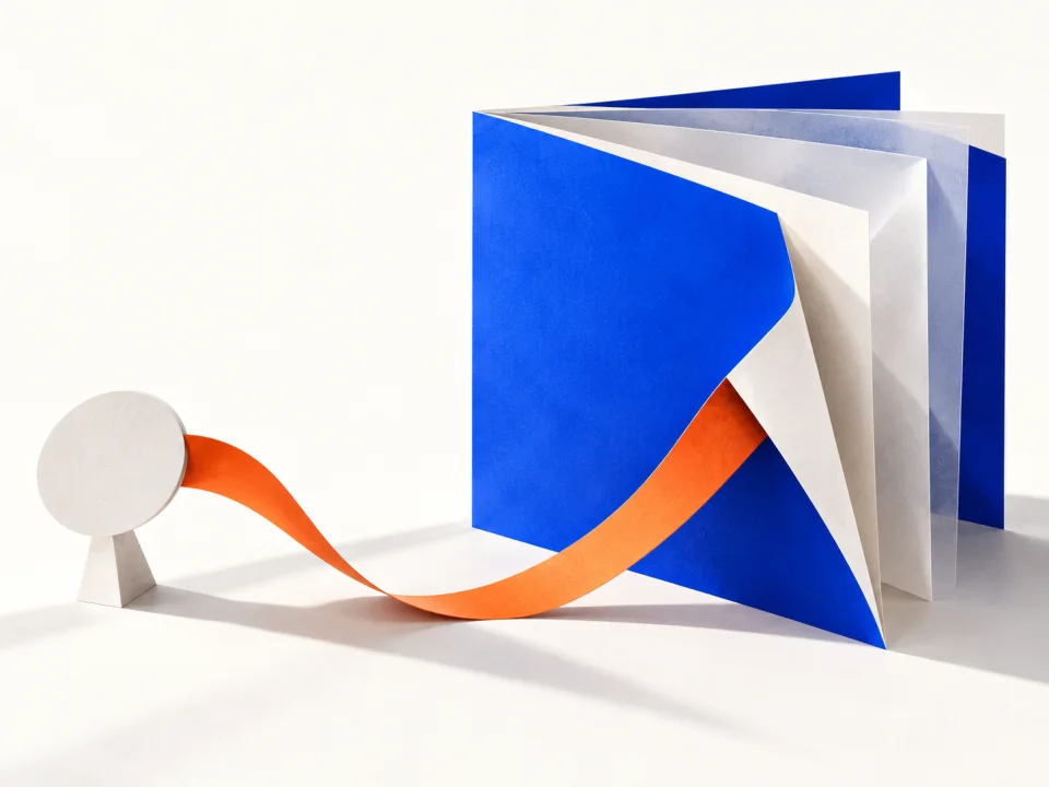 A small paper disc linked by an orange ribbon to a standing cobalt booklet.