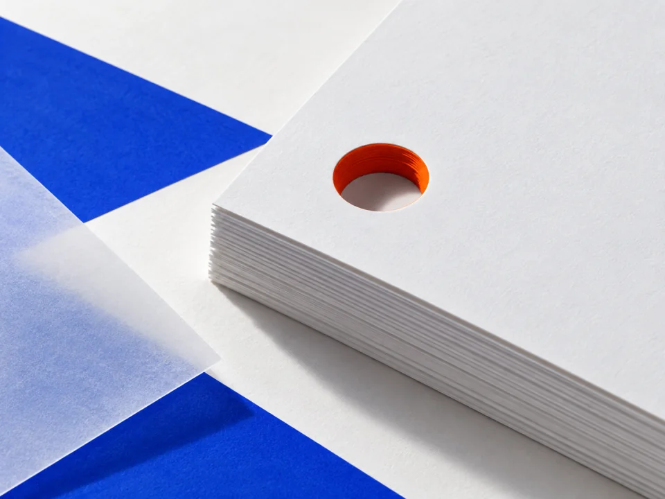 A hole punched through only the top sheets of a deep paper stack, its edge lined orange.