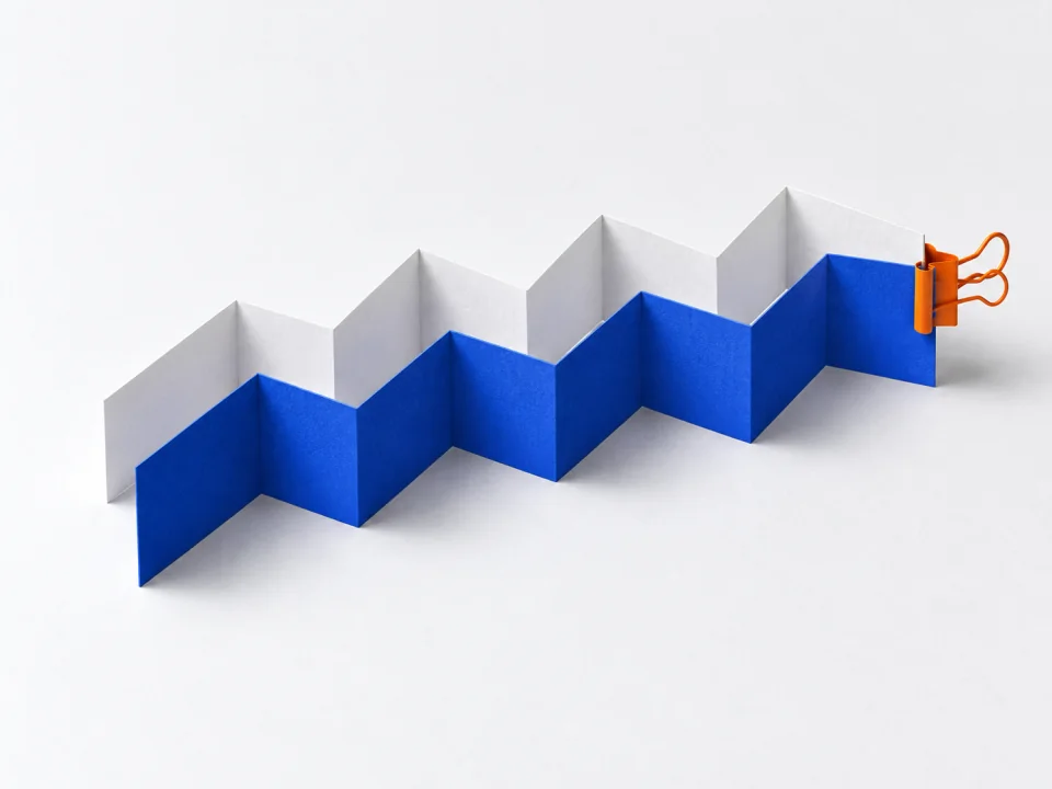 White and cobalt concertina strips folded side by side, joined by an orange clip at the end.