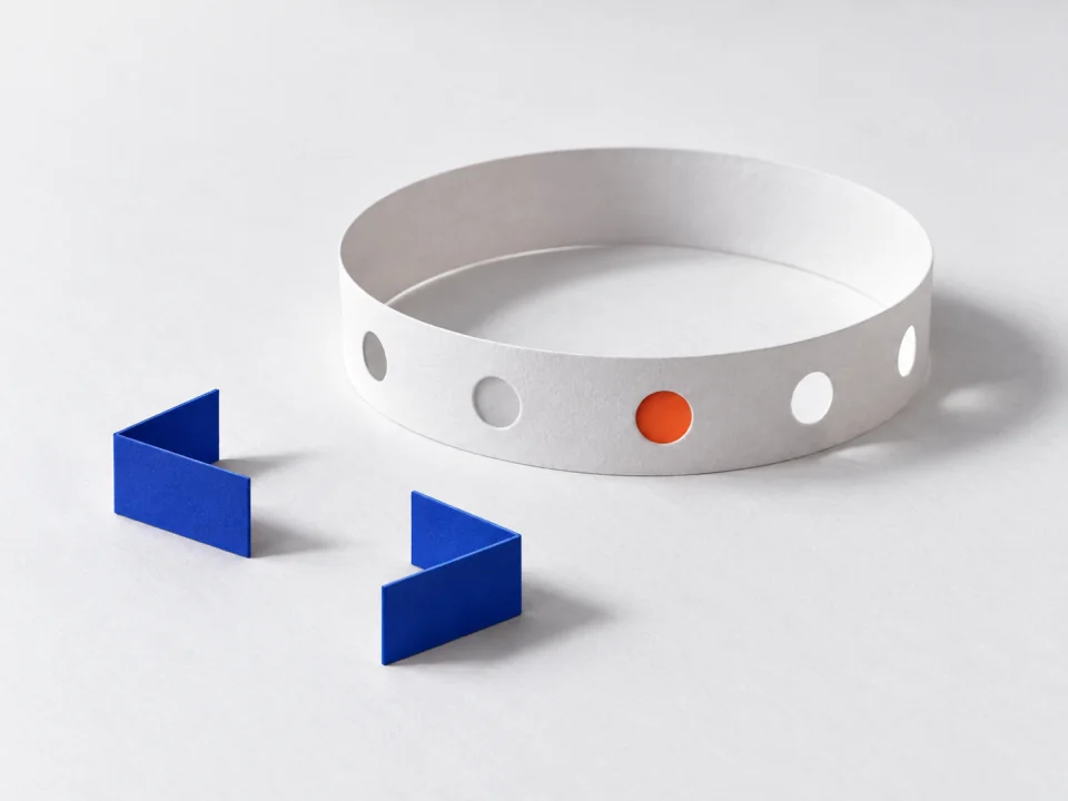 A paper loop with punched holes, one backed in orange, beside two loose cobalt connectors.