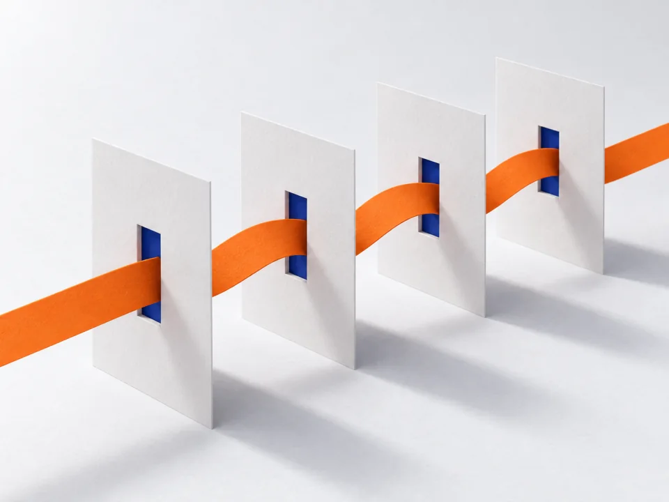 An orange paper ribbon threaded through slits in four standing white sheets.