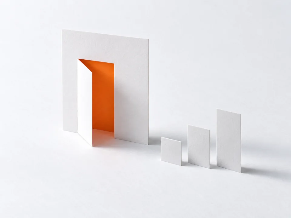 An open flap with an orange inner face cut in a white sheet, beside three paper tabs.